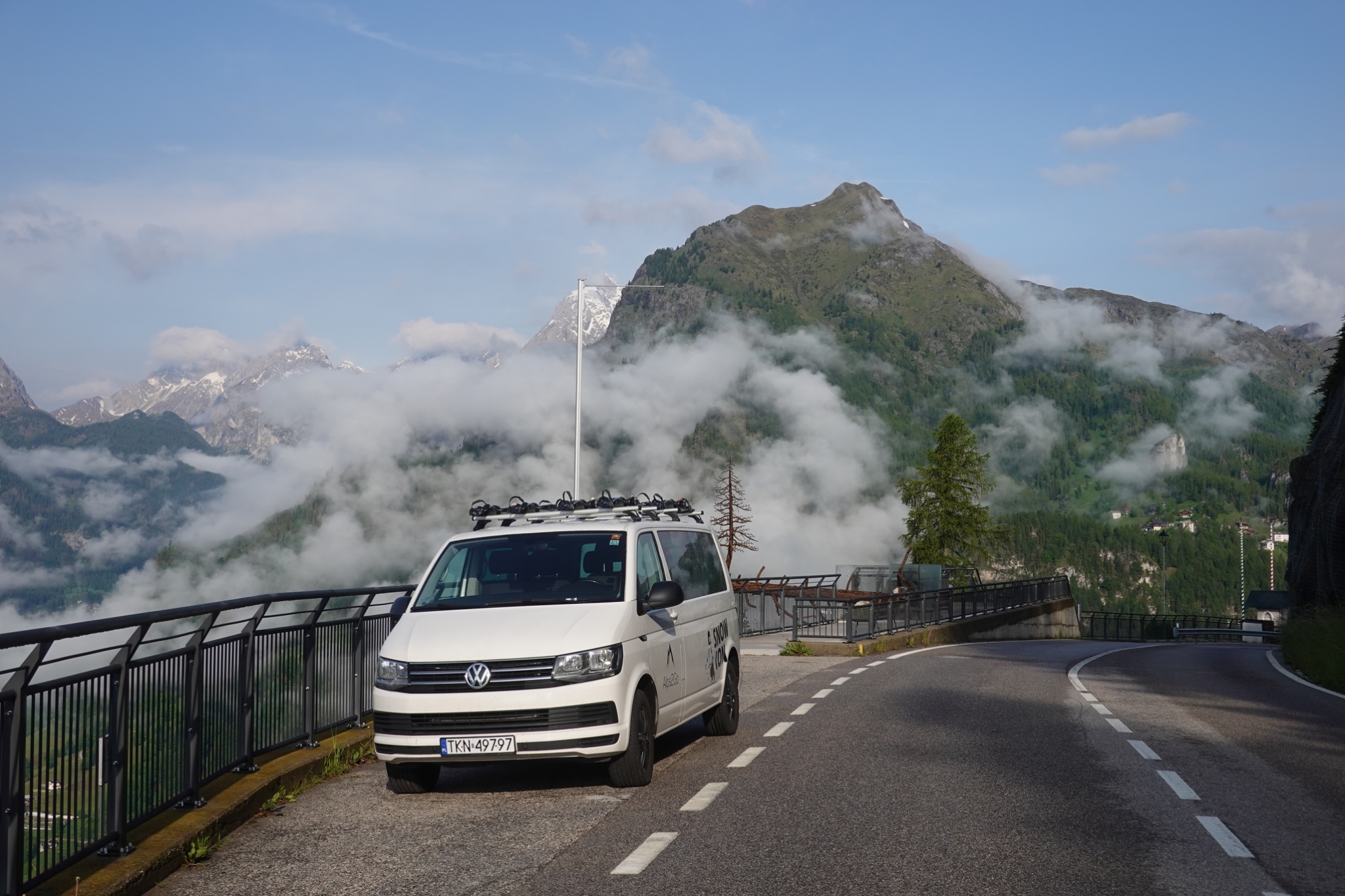Alps2Go support van parked on a mountain road above a cloud-filled valley