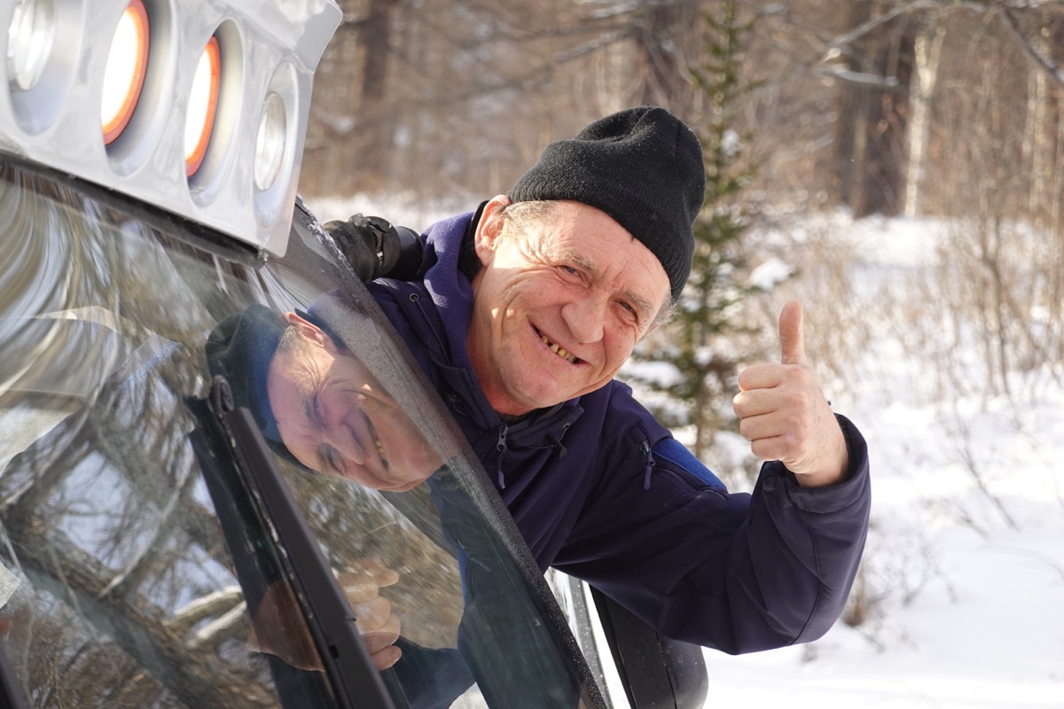 A smiling man beside a snowcat in the forest