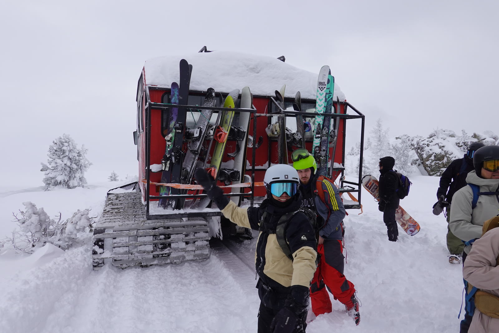 Skiers beside a snowcat loaded with skis and snowboards
