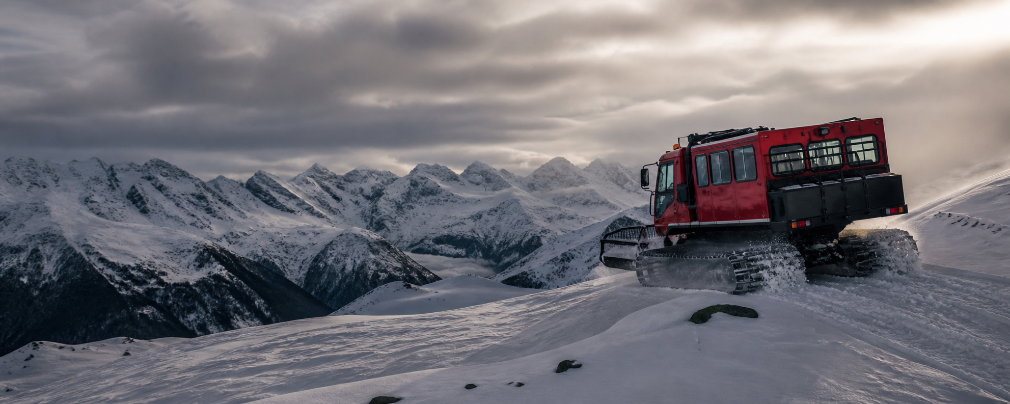Red passenger snowcat crossing a remote snow-covered mountain ridge